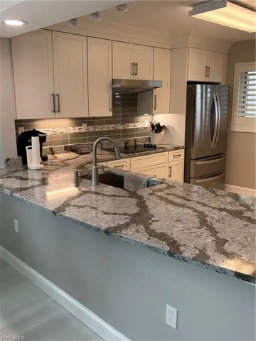 Kitchen featuring white cabinetry, stone counters, range hood, kitchen peninsula, and refrigerator
