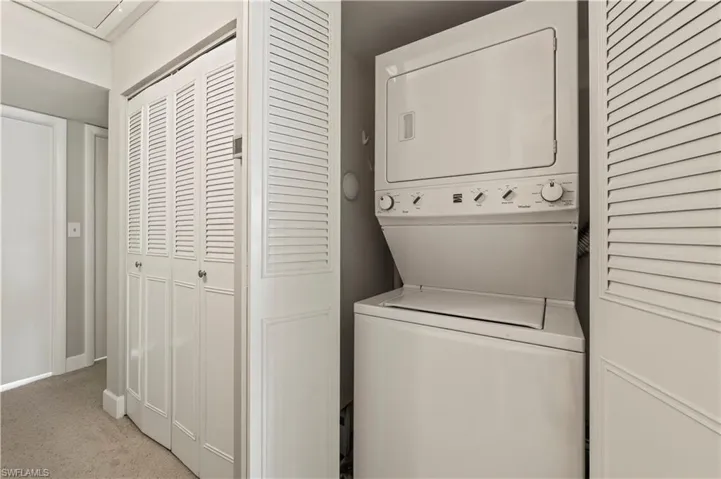 Washroom with stacked washer and clothes dryer and light colored carpet