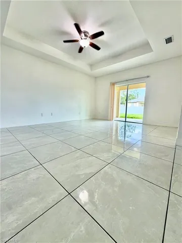 Recessed tray ceiling with a ceiling fan, white walls, and large format tile flooring