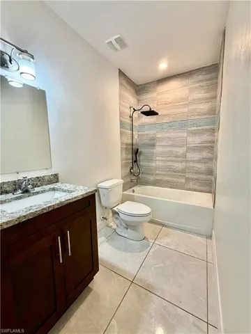 Full bathroom featuring a dark wood-finish vanity with granite countertop, a bathtub with a tiled surround, a toilet, and large format floor tiling