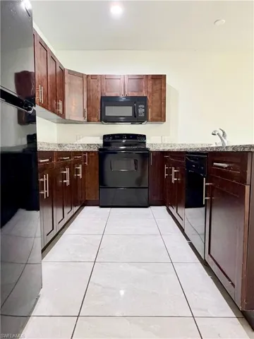 U-shaped kitchen with wood-finish cabinetry, light-toned countertops, tile flooring, and integrated black appliances