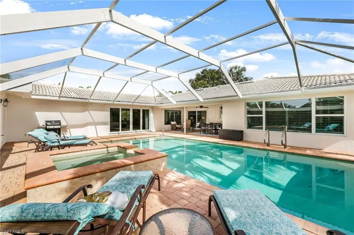 View of swimming pool with an in ground hot tub, a patio area, glass enclosure, and area for grilling
