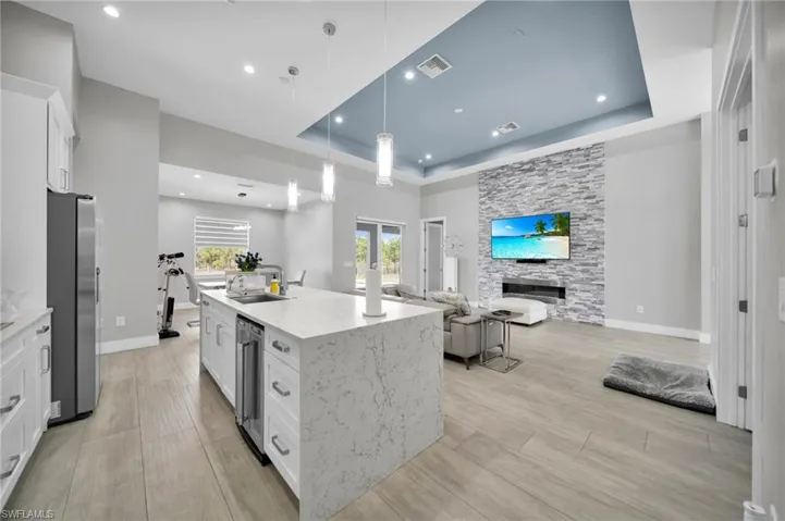 Kitchen featuring white cabinetry, light stone countertops, pendant lighting, a center island with sink, and open floor plan