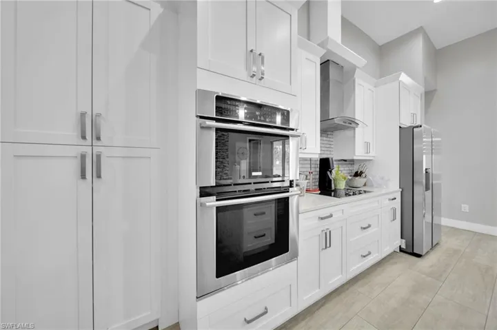 Kitchen with stainless steel appliances, white cabinets, backsplash, and light stone counters