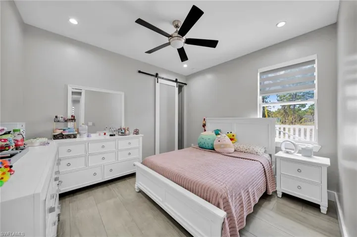 Bedroom featuring a barn door, ceiling fan, light wood-style flooring, and recessed lighting