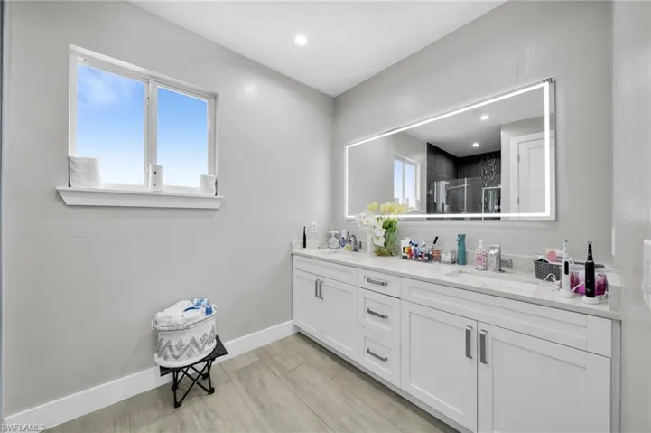 Full bath featuring a stall shower, double vanity, healthy amount of natural light, wood finish floors, and recessed lighting