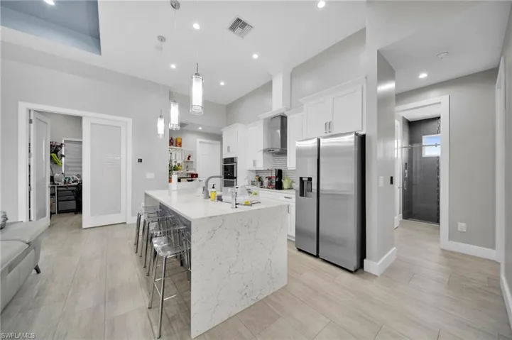 Kitchen with stainless steel appliances, white cabinetry, a kitchen breakfast bar, light stone countertops, and a center island with sink