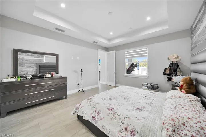 Bedroom with light wood-style flooring, recessed lighting, and a tray ceiling