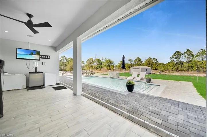 Fenced backyard with an outdoor pool, a patio area, ceiling fan, an outdoor structure, and exterior kitchen