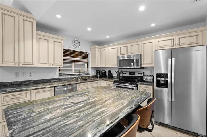Kitchen with cream cabinets, dark stone countertops, stainless steel appliances, light tile patterned flooring, and recessed lighting