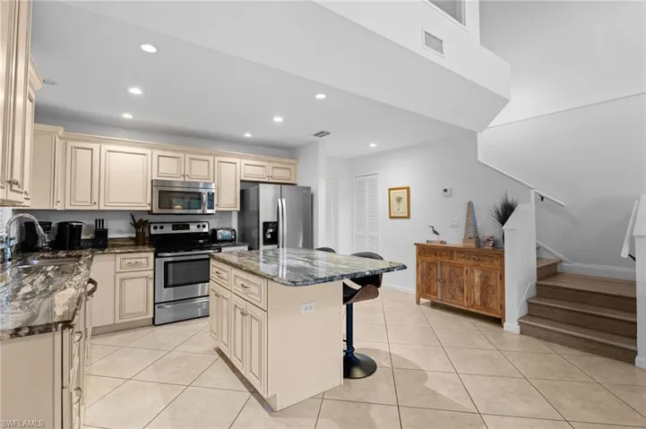 Kitchen featuring cream cabinets, dark stone countertops, stainless steel appliances, a kitchen bar, and recessed lighting