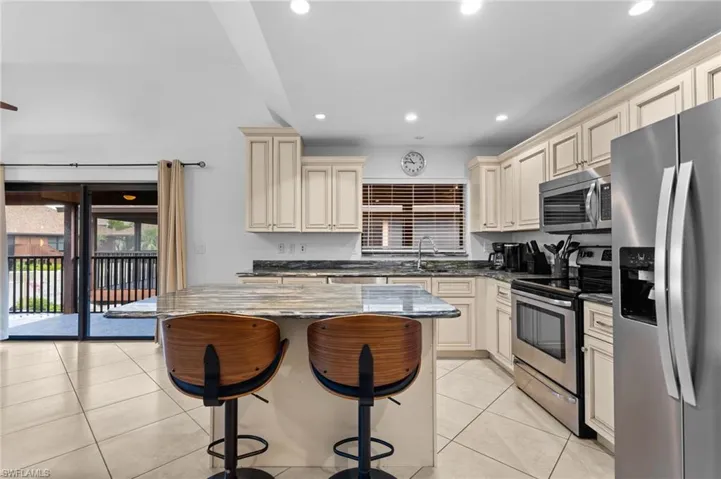 Kitchen featuring cream cabinets, dark stone counters, stainless steel appliances, a kitchen breakfast bar, and recessed lighting