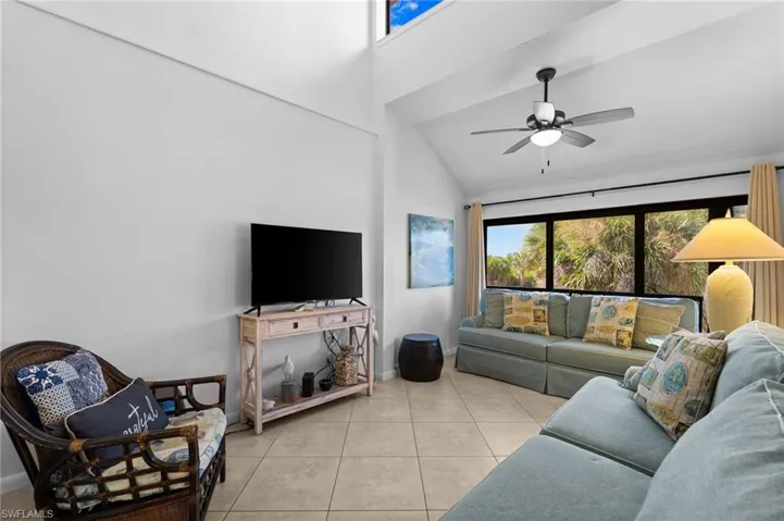 Living room with healthy amount of natural light, light tile patterned floors, high vaulted ceiling, and a ceiling fan