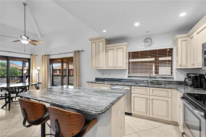 Kitchen with cream cabinetry, dark stone countertops, a kitchen bar, light tile patterned floors, and stainless steel appliances