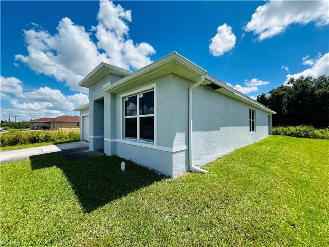 View of side of property with a yard, stucco siding, concrete driveway, and a garage