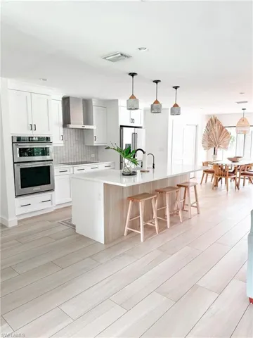 Kitchen with stainless steel appliances, backsplash, hanging light fixtures, a kitchen island with sink, and wall chimney exhaust hood