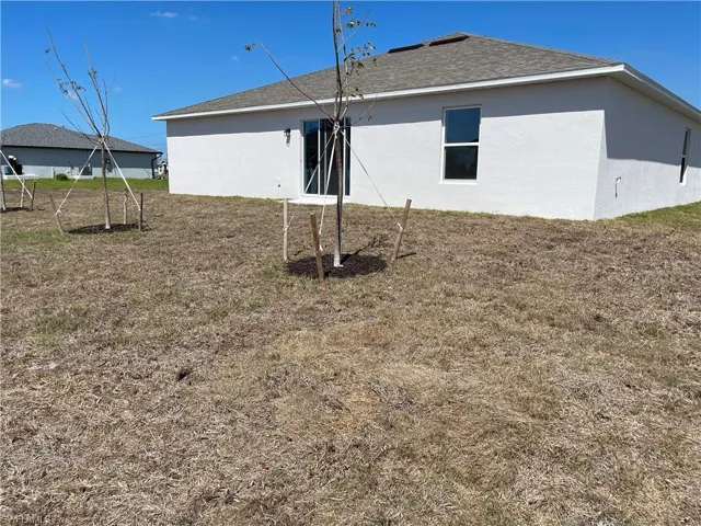 Back of house with stucco siding, roof with shingles, and a lawn