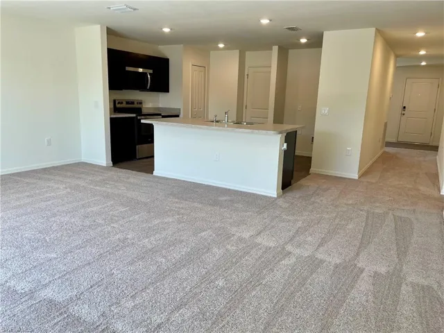 Kitchen with light countertops, stainless steel appliances, a kitchen island with sink, light carpet, and recessed lighting