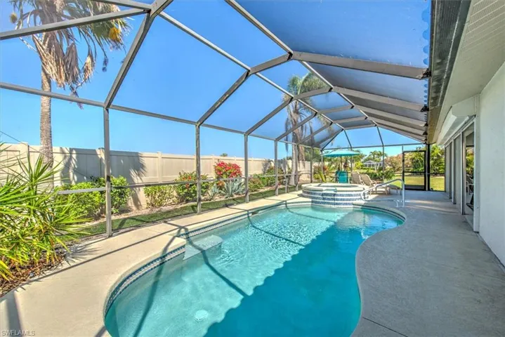 View of pool with glass enclosure, a patio, a pool with connected hot tub, and fence