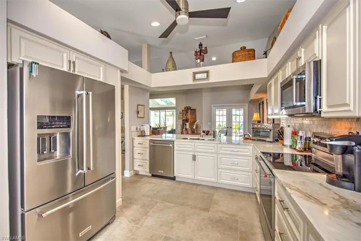 Kitchen featuring a sink, stainless steel appliances, white cabinets, french doors, and tasteful backsplash
