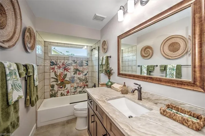 Full bathroom with tile patterned floors, visible vents, toilet,  shower combination, and vanity