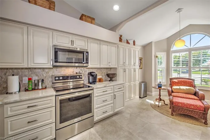 Kitchen featuring backsplash, appliances with stainless steel finishes, pendant lighting, and lofted ceiling
