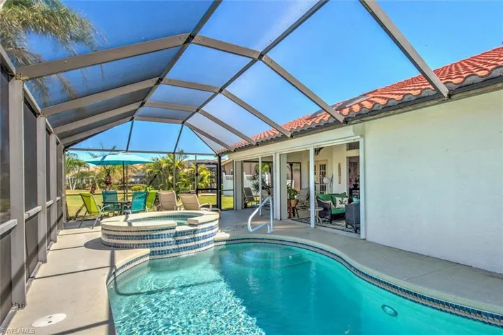View of pool with glass enclosure, a pool with connected hot tub, and a patio