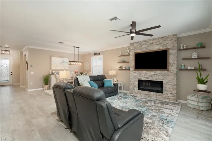 Tiled living room with a fireplace, a healthy amount of sunlight, ornamental molding, and ceiling fan