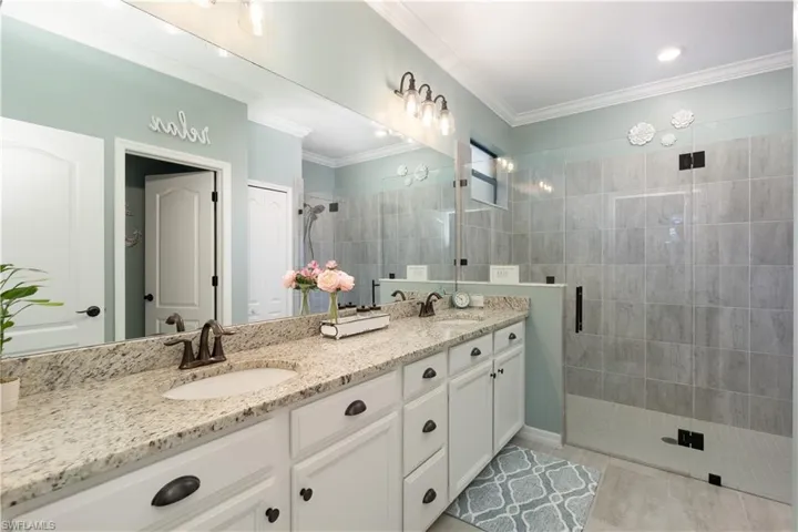 Bathroom featuring tile patterned flooring, dual vanity, ornamental molding, and an enclosed shower