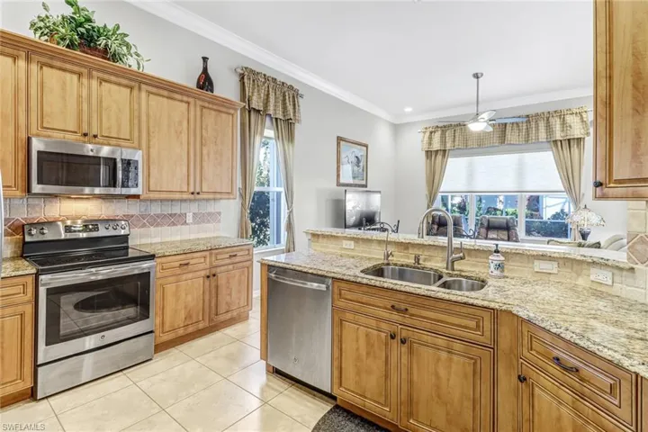 Kitchen with light stone counters, stainless steel appliances, tasteful backsplash, sink, and light tile floors
