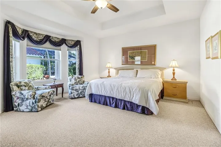 Carpeted bedroom featuring ceiling fan and a raised ceiling