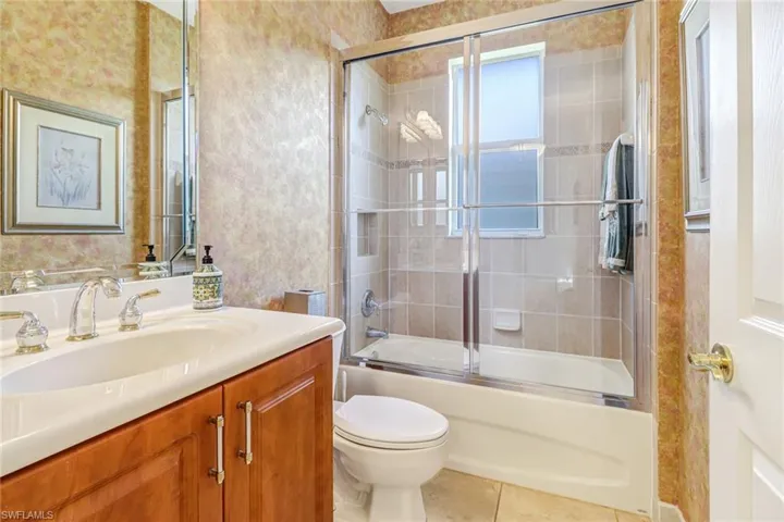 Full bathroom with tile floors, shower / bath combination with glass door, vanity, and toilet