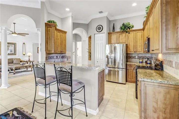 Kitchen with stainless steel appliances, a breakfast bar area, backsplash, ceiling fan, and light tile floors