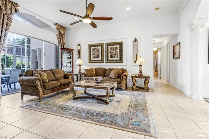 Tiled living room featuring ceiling fan, crown molding, and decorative columns