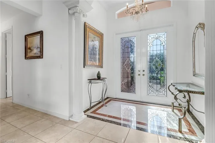 Entrance foyer featuring a notable chandelier, french doors, decorative columns, and light tile flooring
