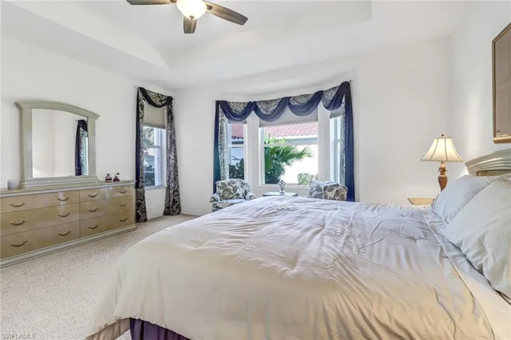 Bedroom with ceiling fan, a raised ceiling, and light colored carpet