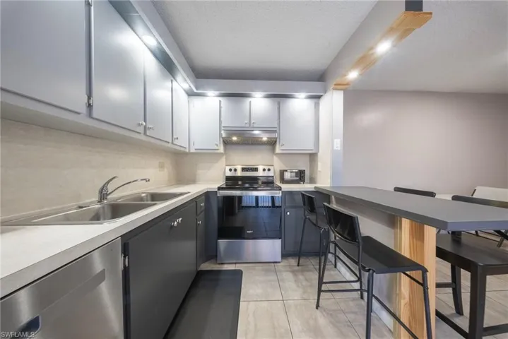 Kitchen featuring stainless steel appliances, light countertops, a kitchen bar, a textured ceiling, and dual tone cabinetry