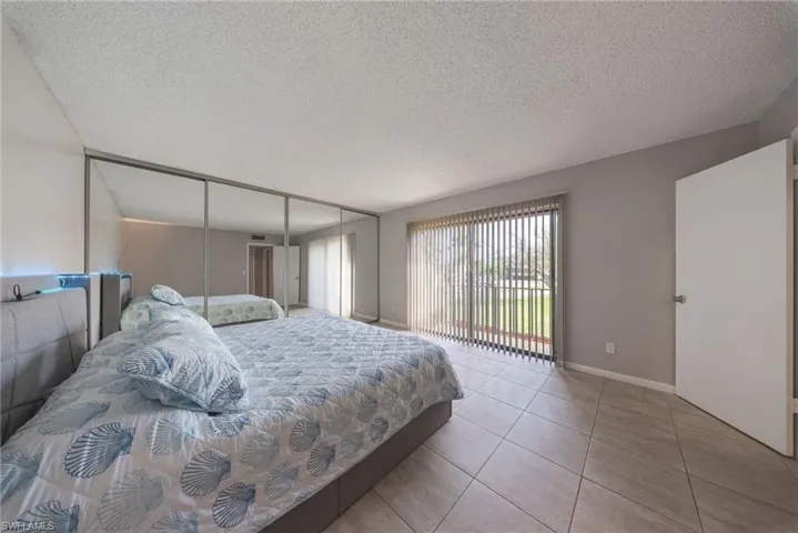 Bedroom with a textured ceiling, light tile patterned flooring, access to outside, and a closet