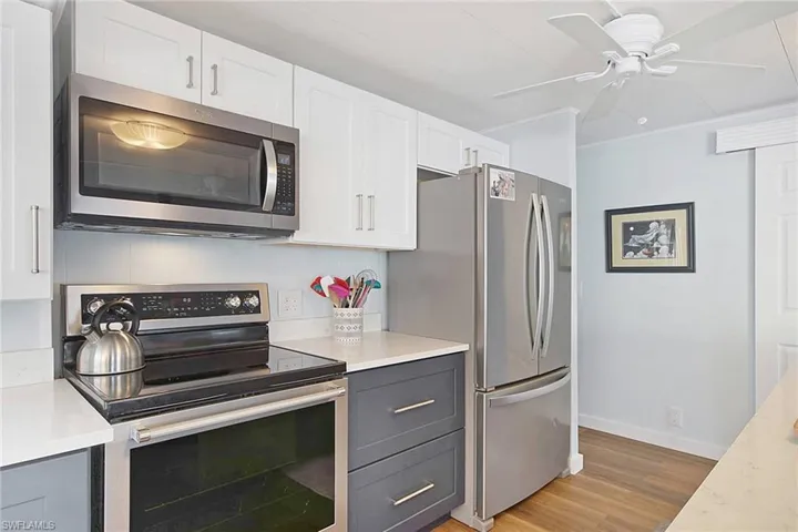 Kitchen with appliances with stainless steel finishes, backsplash, ceiling fan, white and dark blue cabinets, and light wood-style floors