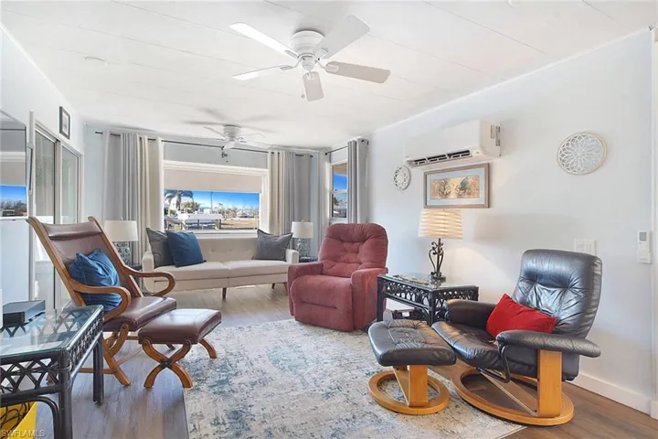 Living area with ceiling fan, wood-type flooring, and a wall unit AC