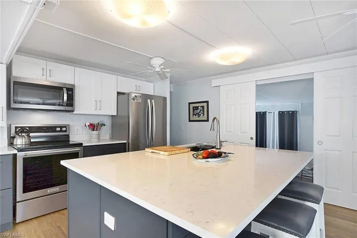 Kitchen with a kitchen island with sink, white and dark blue cabinets, stainless steel appliances, and light wood-style floors