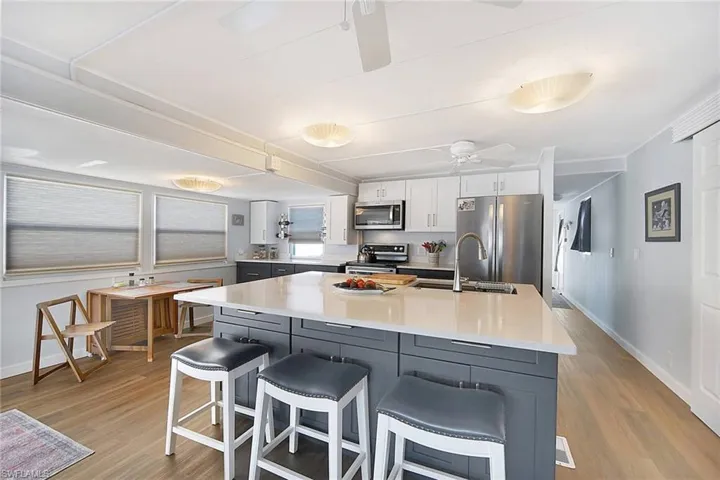 Kitchen with white and dark blue cabinets, sink, light wood-style floors, appliances with stainless steel finishes, and a kitchen island.