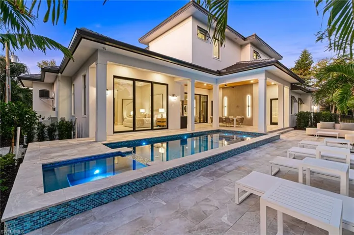 Back house at dusk with a patio, outdoor lounge area, and a swimming pool with hot tub