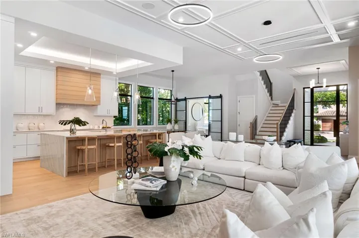 Living room with light hardwood / wood-style floors, a healthy amount of sunlight, a notable chandelier, and coffered ceiling
