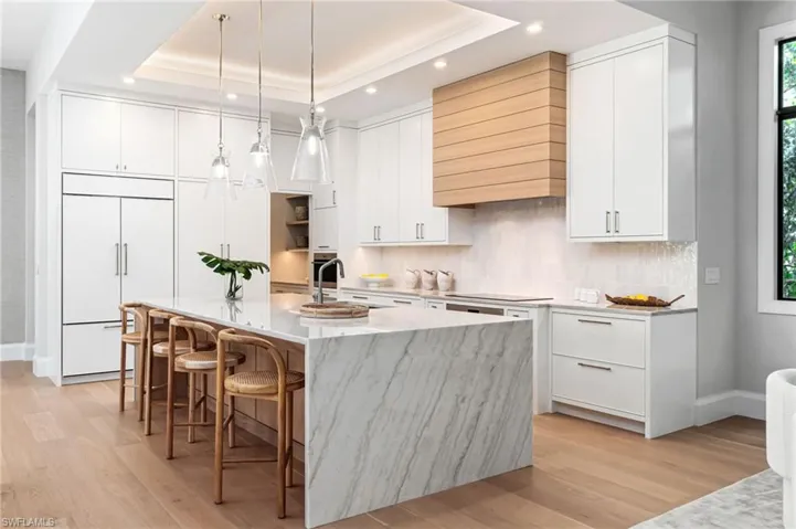 Kitchen featuring white cabinetry, a tray ceiling, paneled built in fridge, and an island with sink