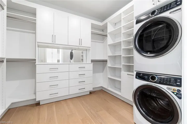 Clothes washing area with stacked washer and dryer, cabinets, and light wood-type flooring