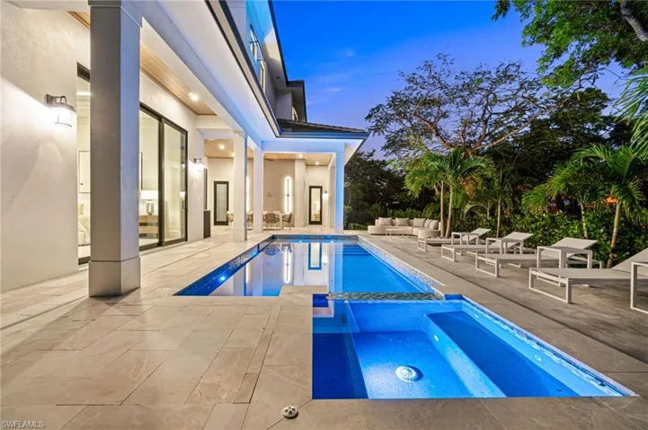Pool at dusk featuring an outdoor hangout area, a patio, and an in ground hot tub