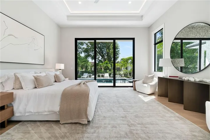 Bedroom with light wood-type flooring, access to outside, and a raised ceiling