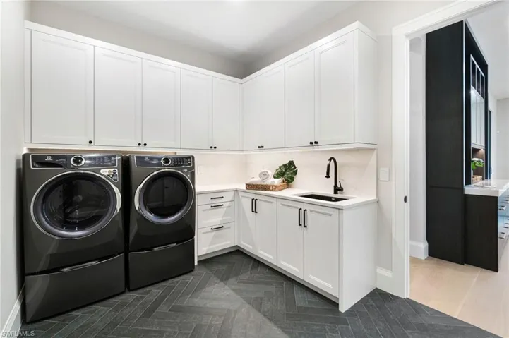 Clothes washing area with cabinets, washing machine and dryer, sink, and dark parquet floors