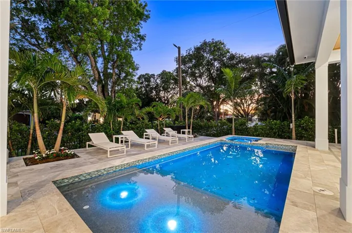 Pool at dusk with an in ground hot tub and a patio area